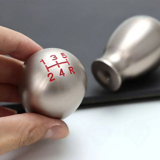 Hand holding metallic teardrop shift knob with red shift pattern